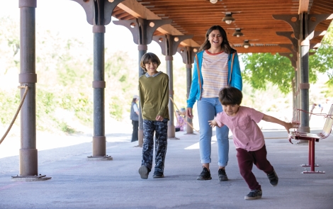 Image of a woman with two sons walking under a park pergola