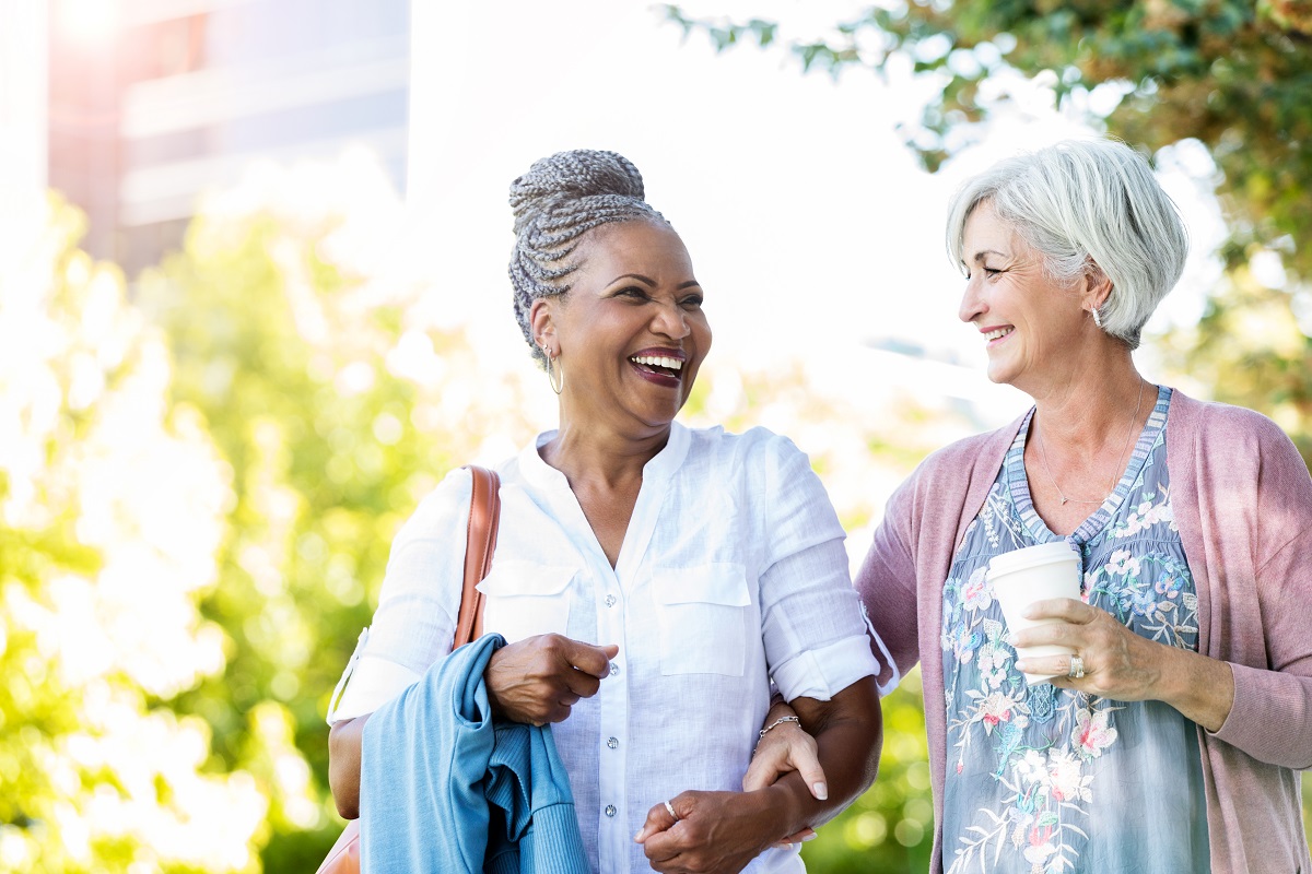 Two women walking down a sunny street ahile talking and laughing